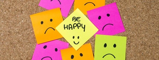 smiley cartoon face expression on yellow post it note surrounded by sad and depressed faces on cork message board in happiness versus depression and smile against adversity concept