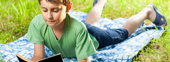 Portrait of a boy reading a book outdoor on the grass