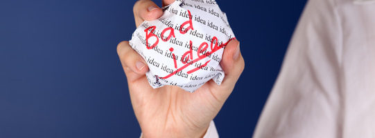 Crumpled paper ball with red words "Bad idea" and background with words "idea" in woman hand.