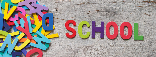 The colorful words "SCHOOL" made with wooden letters next to a pile of other letters over old wooden board.