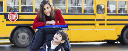 Big sister with disabled brother in wheelchair by school bus